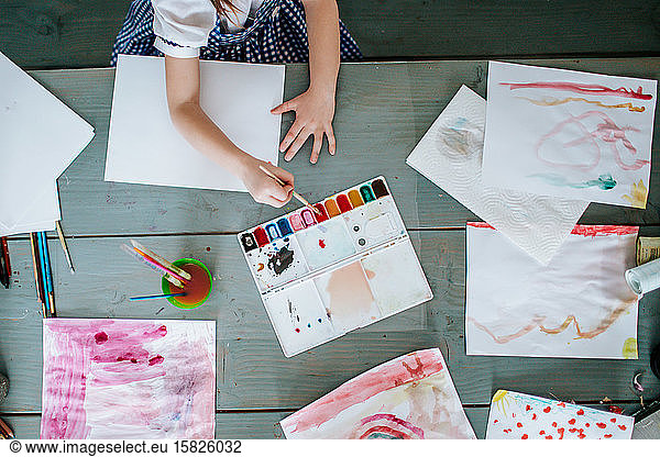 young girl painting bright pictures on a table from above