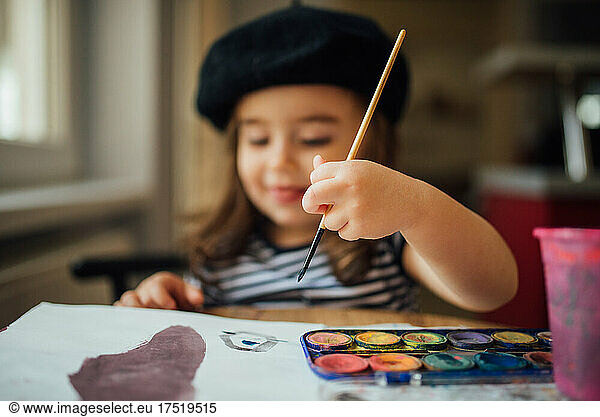 Young girl painting with a brush and watercolors.