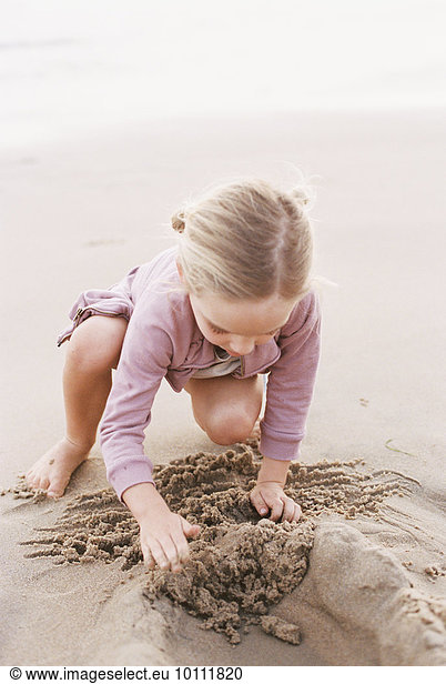 Young girl playing in the sand on a beach by the ocean.