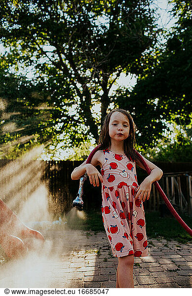 Young girl playing outside with garden hose
