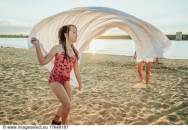 Young girl playing with sheet at the beach on a summer say
