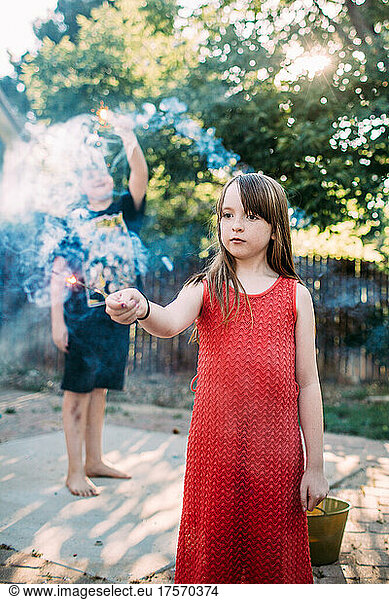 Young girl playing with sparkler outside on summer day