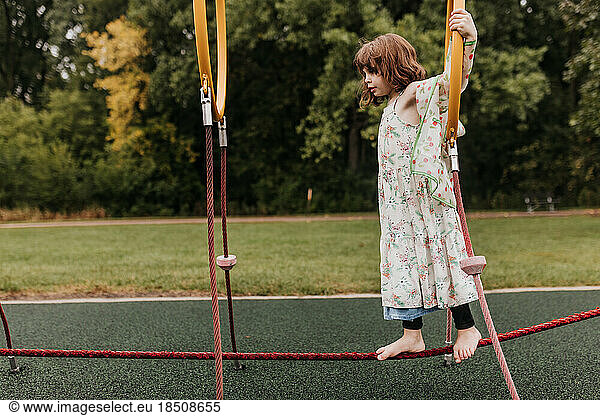 Young girl plays on playground equipment at park on cloudy day
