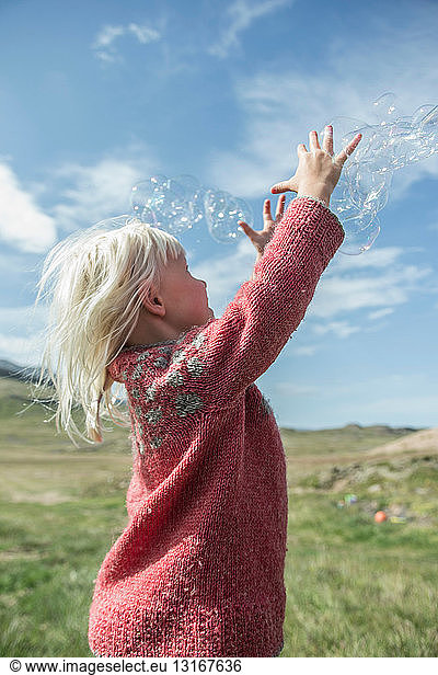 Young girl reaching to catch bubbles
