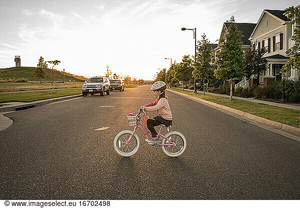 young girl rides a bike across the road at sunset