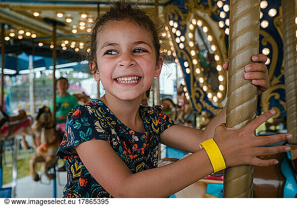 Young girl riding carousel with toothy smile