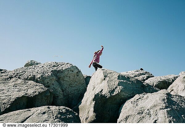 young girl running along large rocks playing in the sunshine
