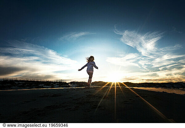 Young girl running towards the sunset under big blue sky