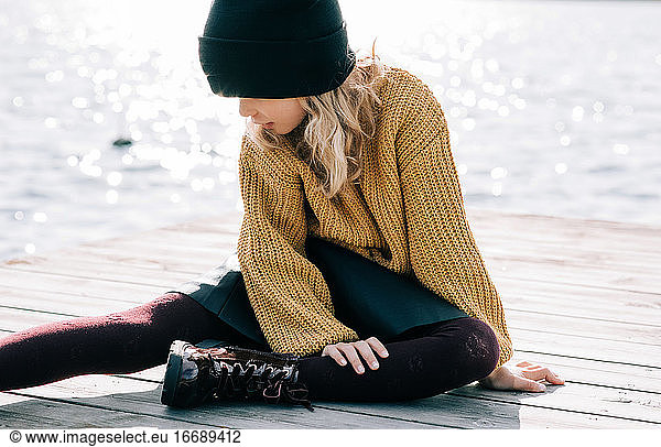 young girl sat by the sea in a fall outfit looking thoughtful