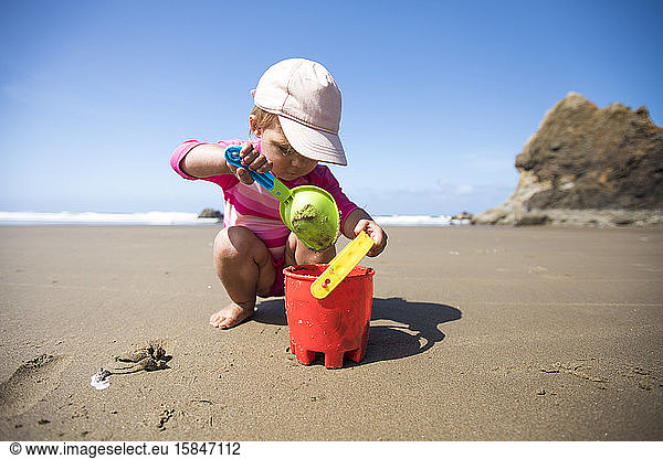 Young girl shovelling sand into bucket at the beach.