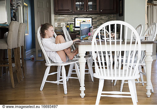 Young Girl Sits at Kitchen Table Doing School Work on Laptop Computer