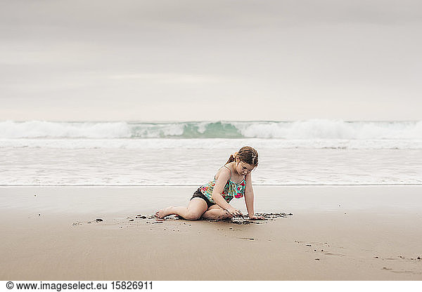Young girl sitting and playing at the beach