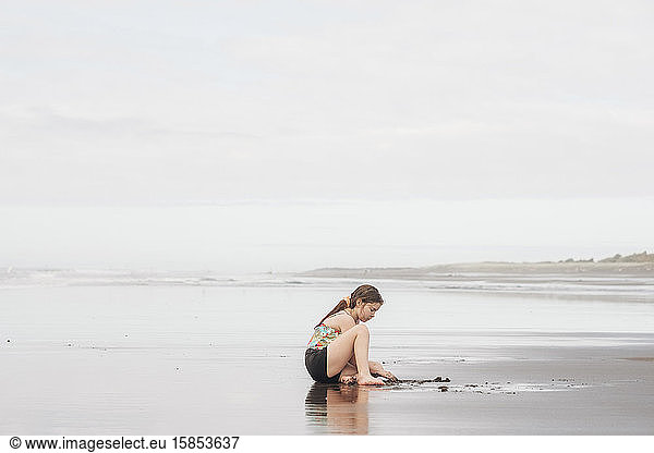 Young girl sitting and playing in the sand at the beach