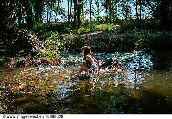Young girl sitting in a calm creek on a summer day