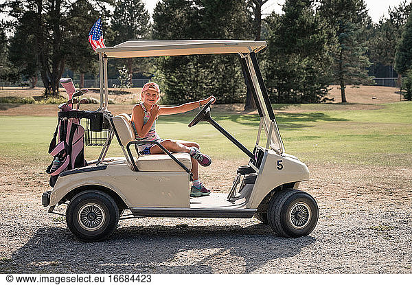 Young Girl Sitting in Golf Cart With Pink Golf Bag on Sunny Day