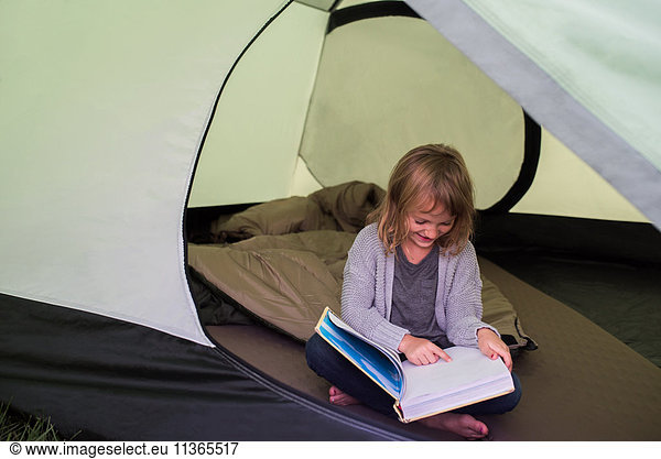 Young girl sitting in tent  reading book