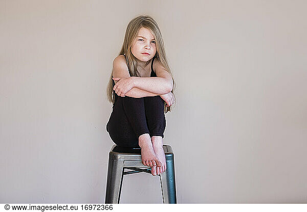 Young girl sitting on a stool inside