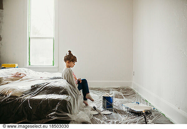 Young girl sitting on bed in freshly painted white room