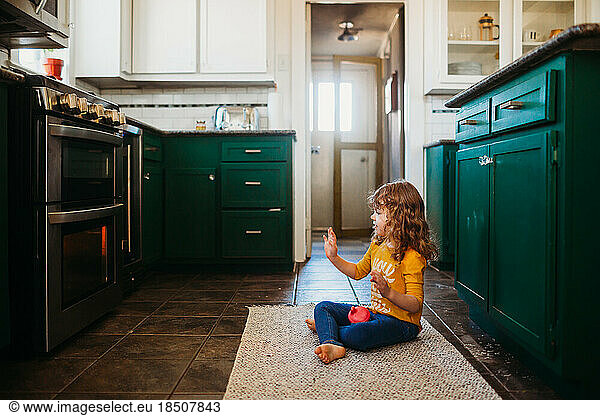 Young girl sitting on floor in kitchen waiting for food to cook