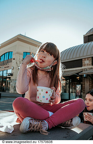 Young girl sitting on ledge eating ice cream