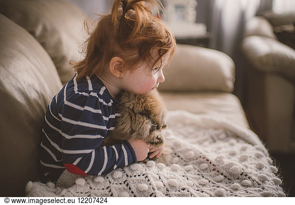 Young girl sitting on sofa  hugging pet dog