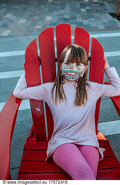 Young girl sitting outside on red chair wearing mask