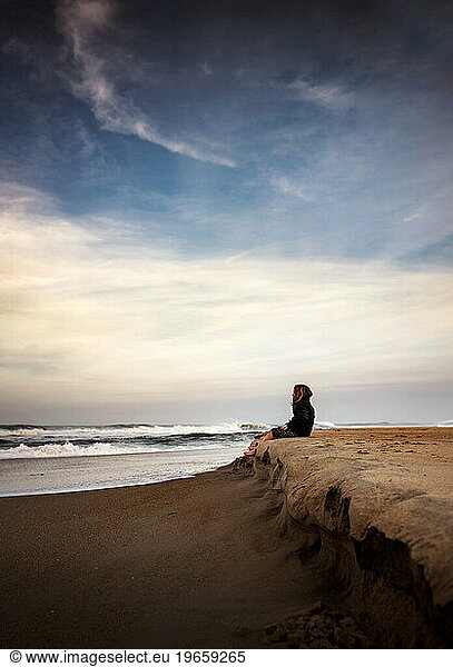 Young girl sitting quietly on the beach at sunset