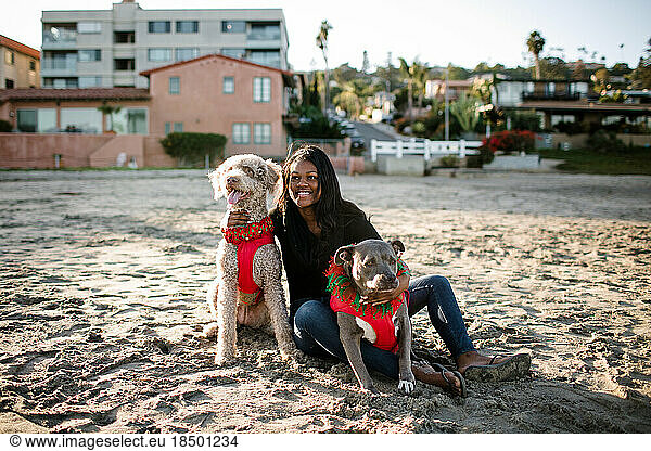 Young girl smiling and hugging dogs on beach at sunset