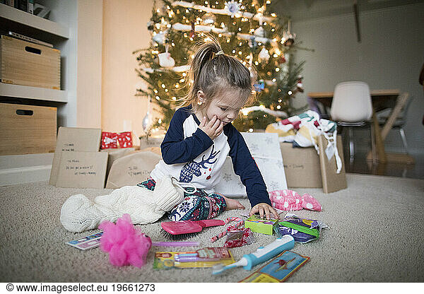 young girl spreads her gifts out under the Christmas Tree