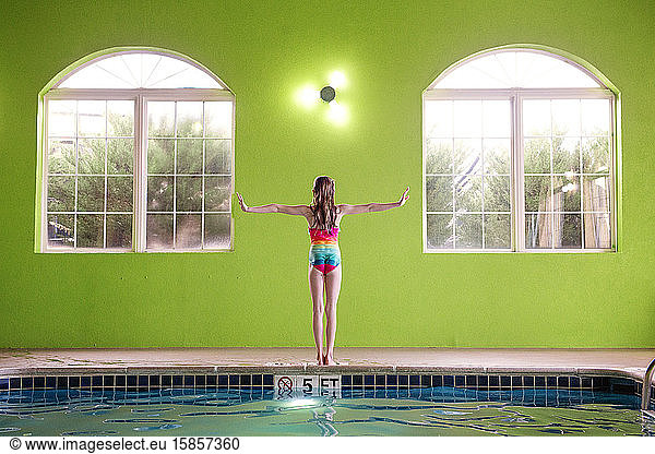 Young Girl Standing on the edge of an Indoor Swimming Pool Arms Out