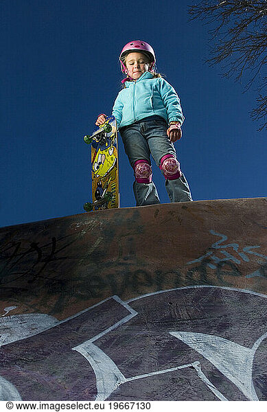 Young girl standing with skateboard looking into skateboard park  Santa Fe  New Mexico.
