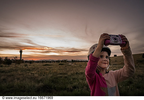young girl takes a selfie with her kid camera with a sunset background