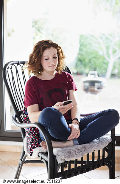 Young girl text messaging while relaxing on armchair at home