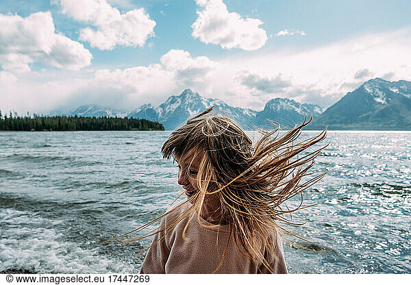 Young girl tossing her hair outside on a sunny day near a lake