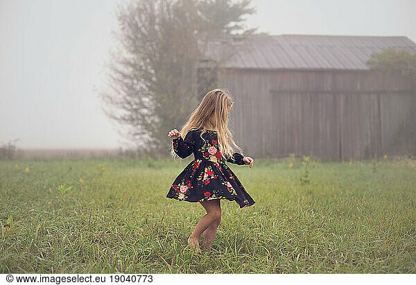 Young girl twirls alone on a foggy morning in an abandoned farm field
