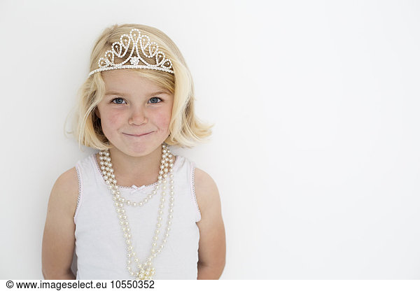 Young girl wearing a tiara and a pearl necklace  posing for a picture in a photographers studio.