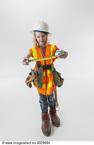 Young girl wearing oversized construction clothes and hard hat holding a tape measure Anchorage alaska united states of america