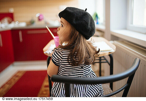 Young girl with a black beret sitting at the kitchen table.