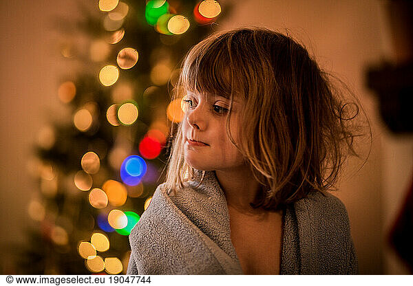 young girl with bedhead draped in blanket in front of christmas tree