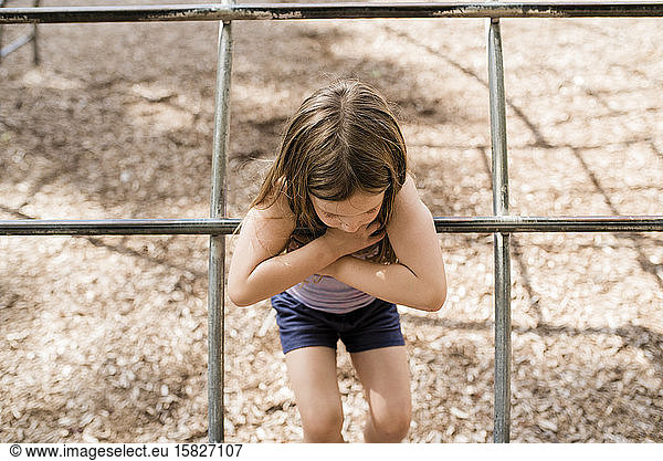 Young girl with brown hair plays on playground in summer on sunny day