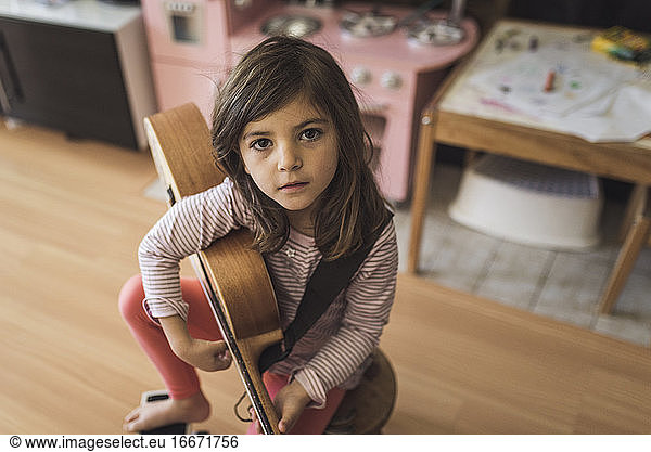 Young girl with deep brown eyes on stool holding small guitar