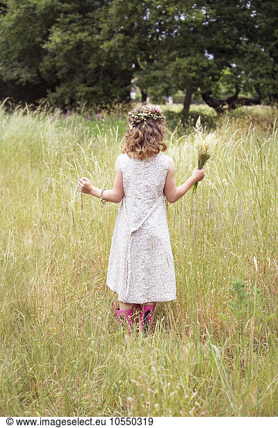 Young girl with flowers in her hair picking wild flowers in a meadow.