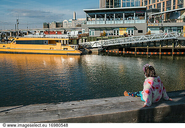 Young girl with tiara watching boats in river harbor
