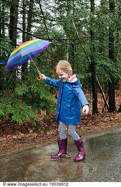 Young girl with umbrella stomps in puddles in the forest