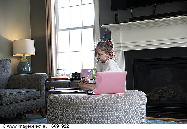 Young Girl Works on Laptop Computer Sitting on Living Room Ottoman