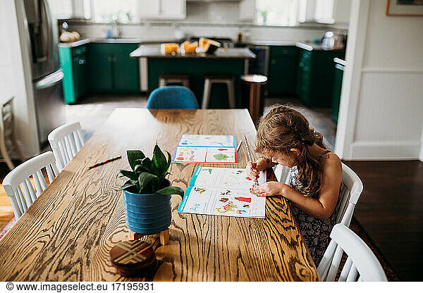 Young girl writing in kindergarten workbook in modern home