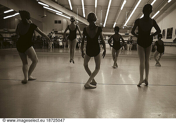 Young girls practicing jumps in front of a mirror in ballet class.