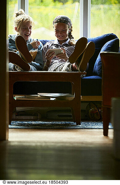 Young girls sitting on a couch looking at a screen and laughing