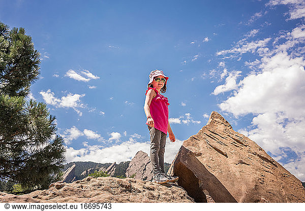 young girls stands on rocks with mountains behind her after hiking