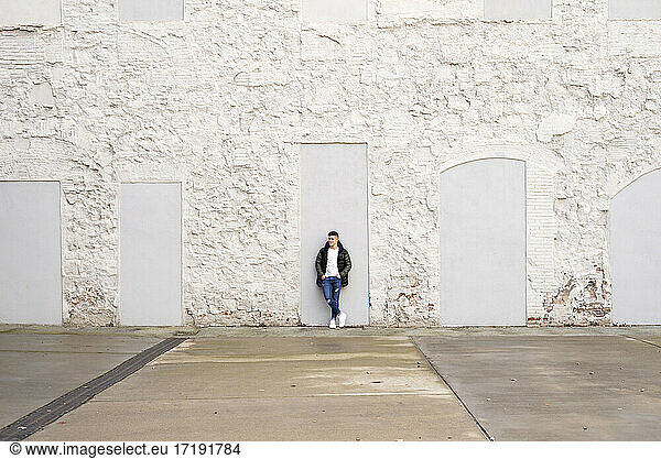 Young guy hands on pocket standing against white wall